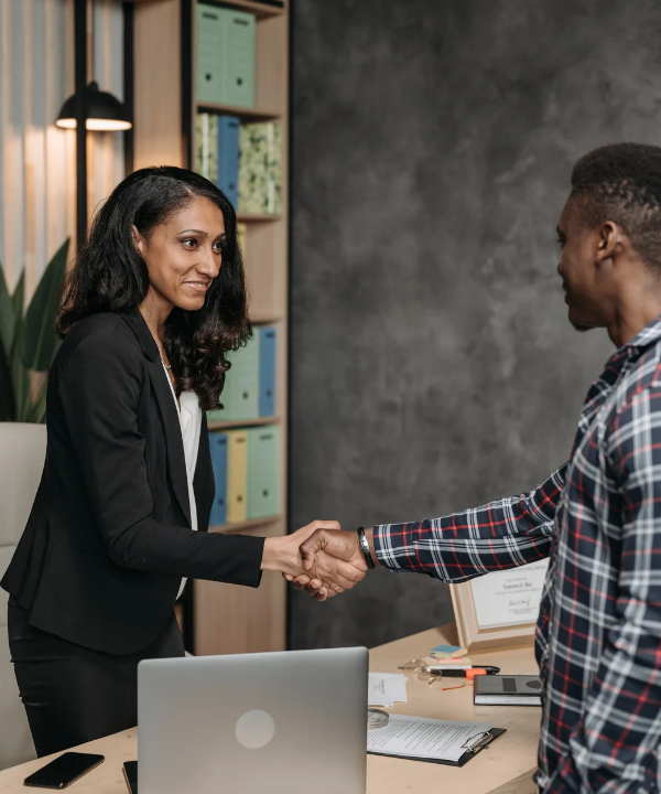 Professional handshake between a woman and man across a desk in an office.