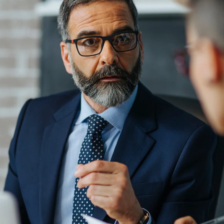 Man in a suit speaking during a serious boardroom discussion.