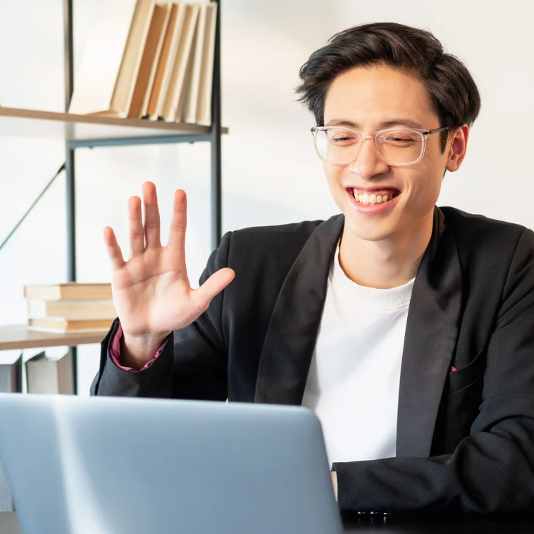 Smiling professional waving during a virtual meeting on a laptop.