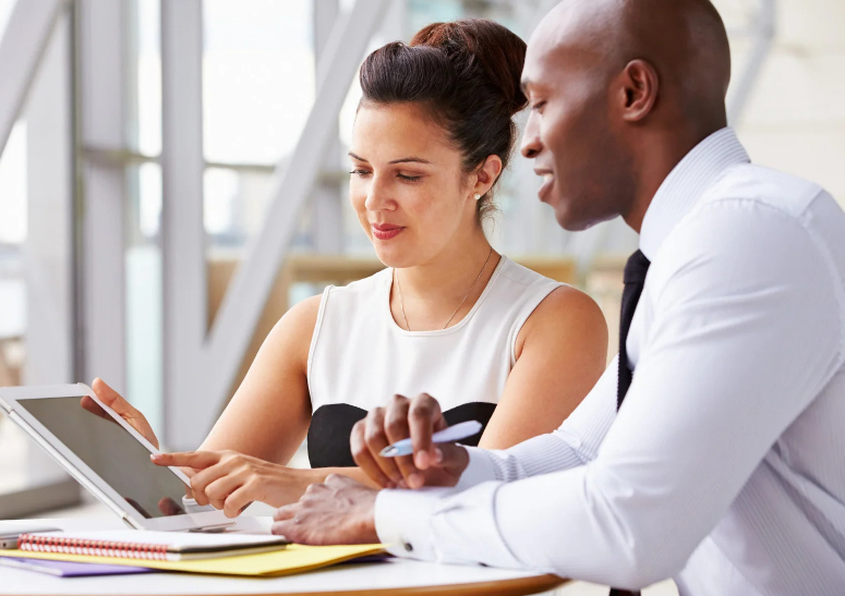 Man and woman discussing business strategy while reviewing notes on a tablet.
